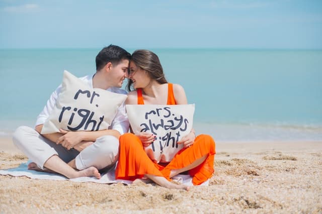 photo man and woman wearing cloths sitting on brown sand near seashore